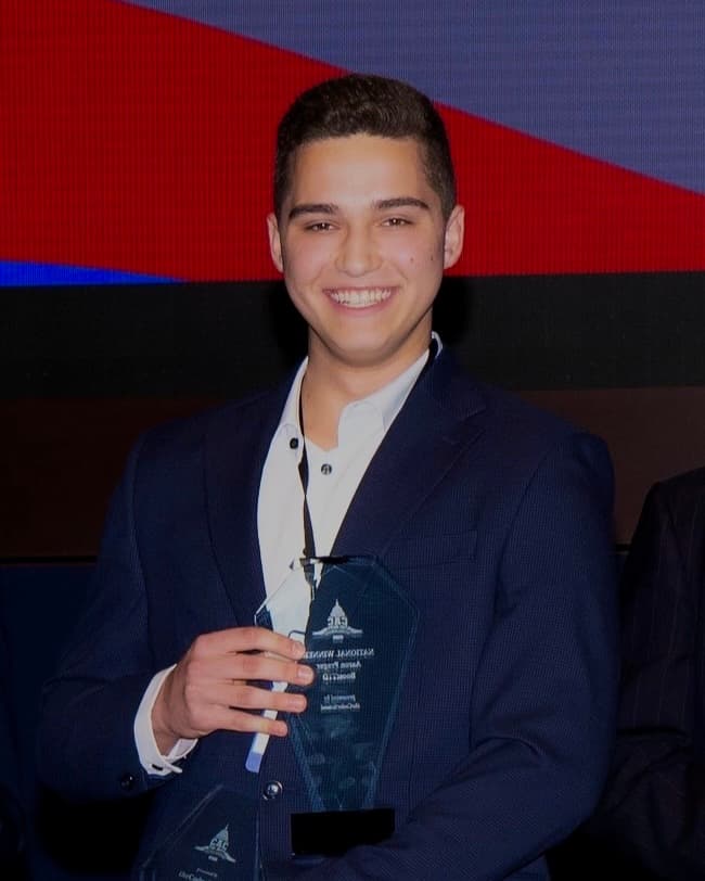 Aaron Prager on stage holding a glass trophy